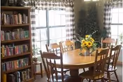 Round wooden dining table with chairs and a sunflower centerpiece in a bright dining room.