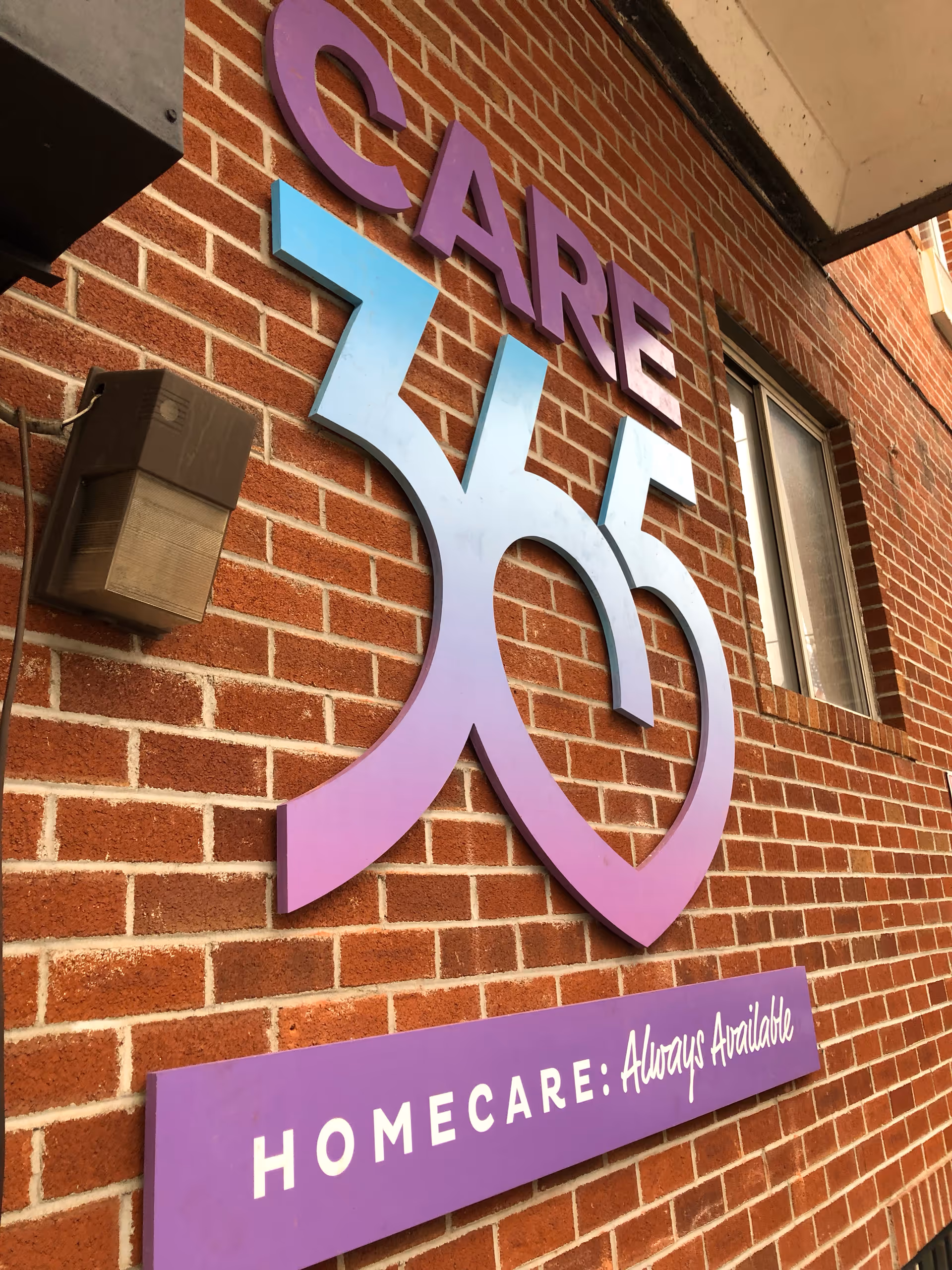 Exterior brick wall with Care365 sign and purple home care branding on building front