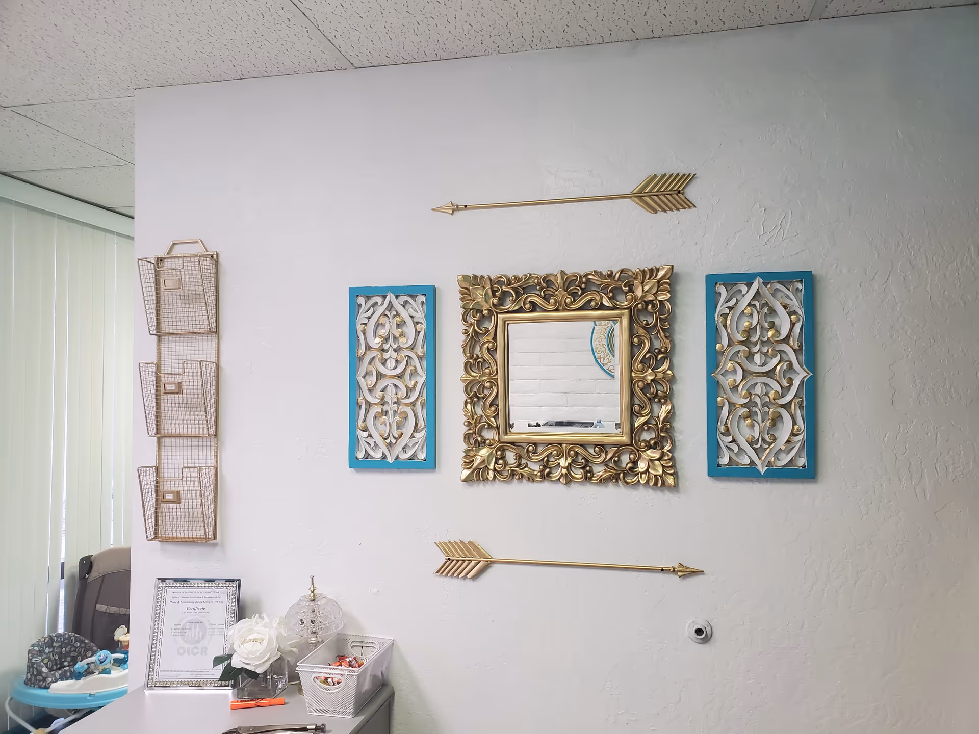 Decorative wall with ornate mirror, blue frames, gold arrows, and storage baskets in a cozy room.