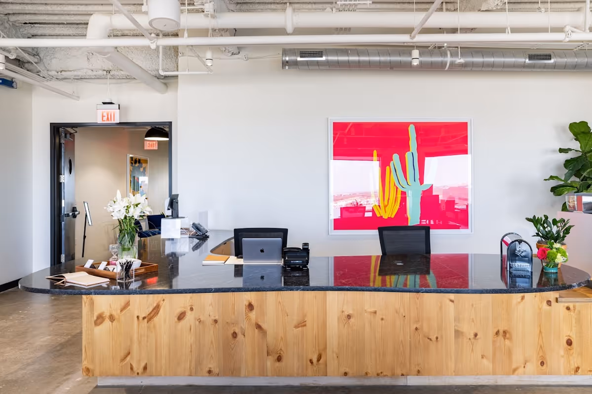 Reception desk with wood base, granite counter, plants, and pink cactus artwork on the wall.