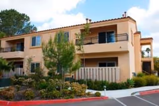 Two-story beige University City Village senior living building with balconies and manicured landscaping.