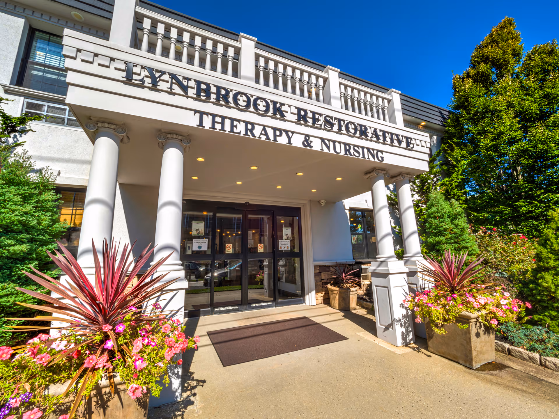 Exterior view of Lynbrook Restorative Therapy and Nursing entrance with columns and planters.