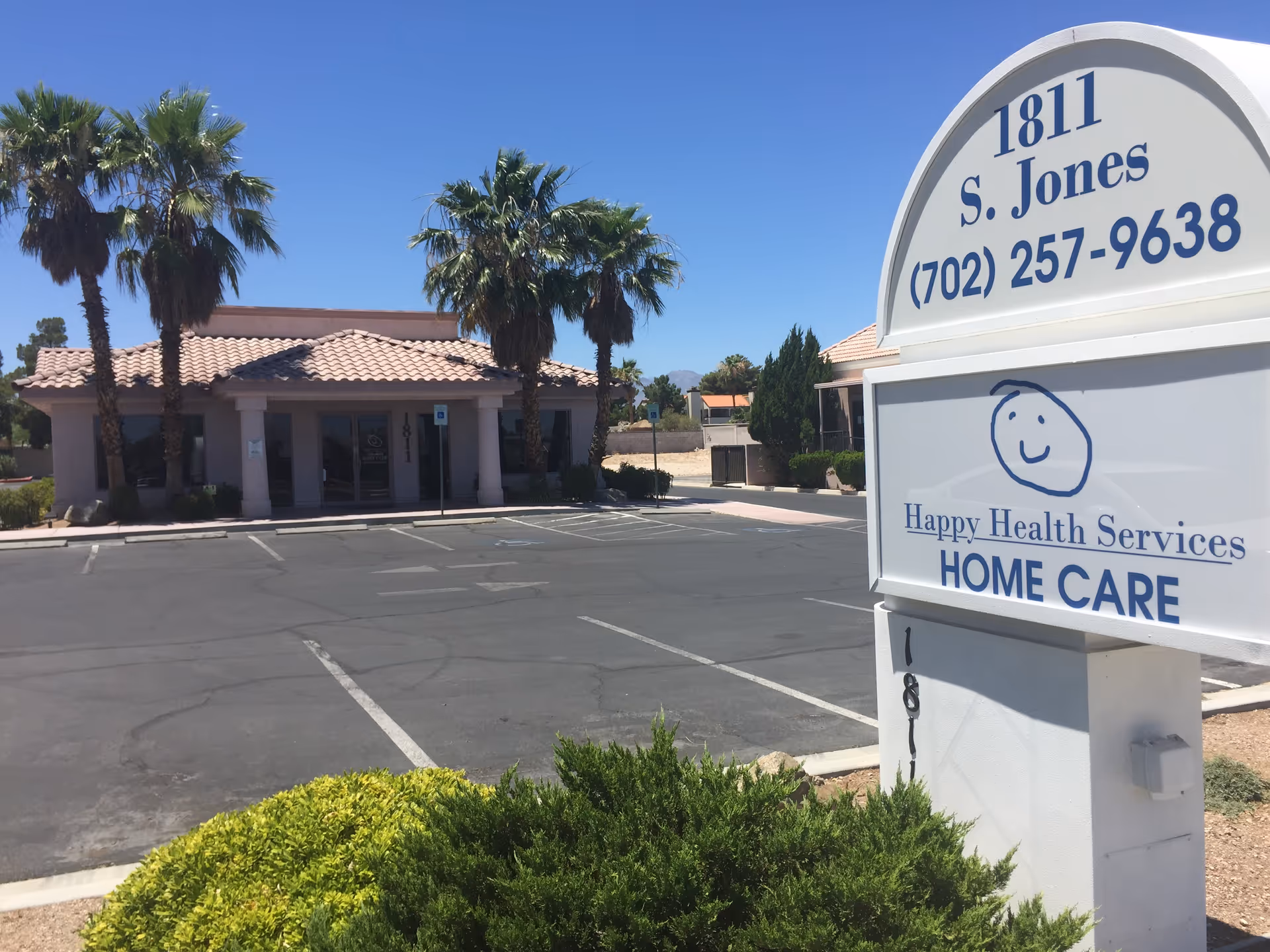 Exterior view of a senior care facility with a large sign and palm trees.