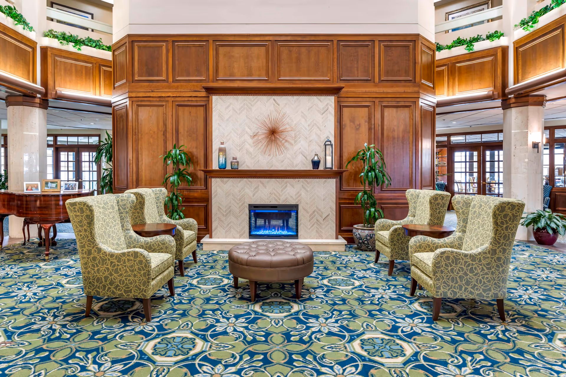 Elegant senior living lobby with a fireplace, wood paneling, and four green armchairs.