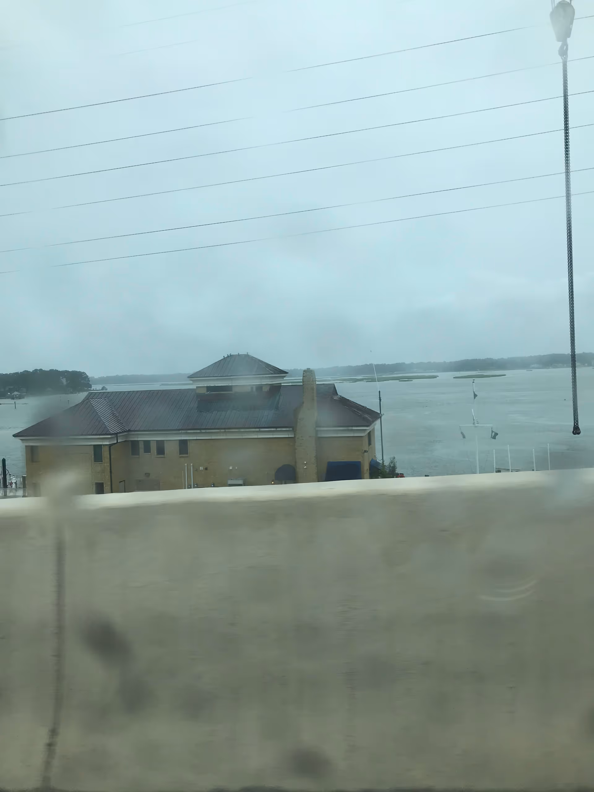 Exterior view of a tan building beside water, seen through a blurred window.