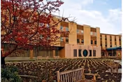 Exterior view of a multi-story nursing home with a courtyard and red-leaved tree.