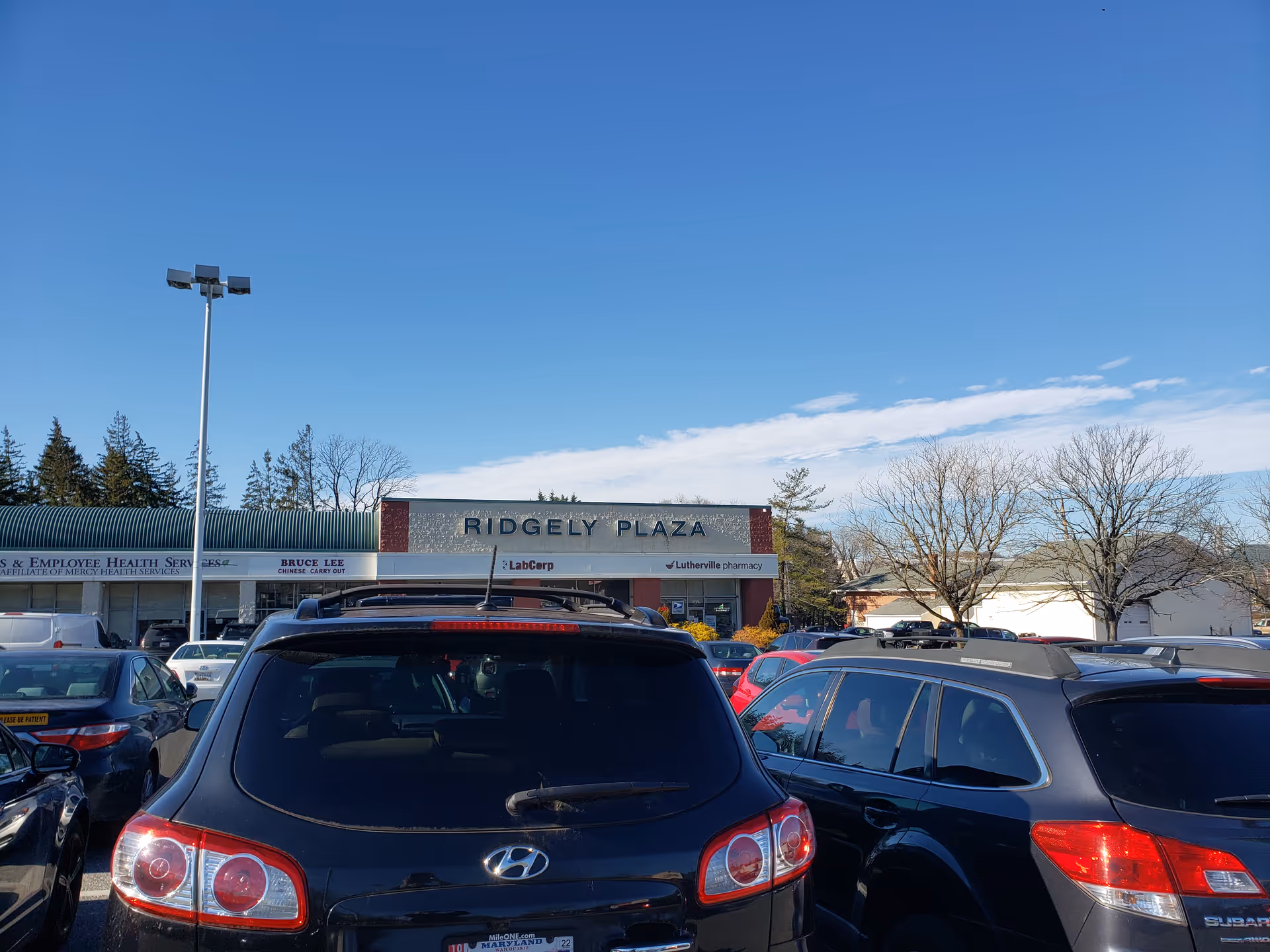 Parking lot in front of Ridgely Plaza storefronts under a clear blue sky