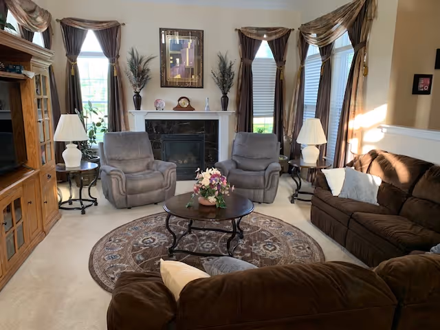 Cozy living room in a senior facility featuring a fireplace, brown seating, and floral centerpiece.