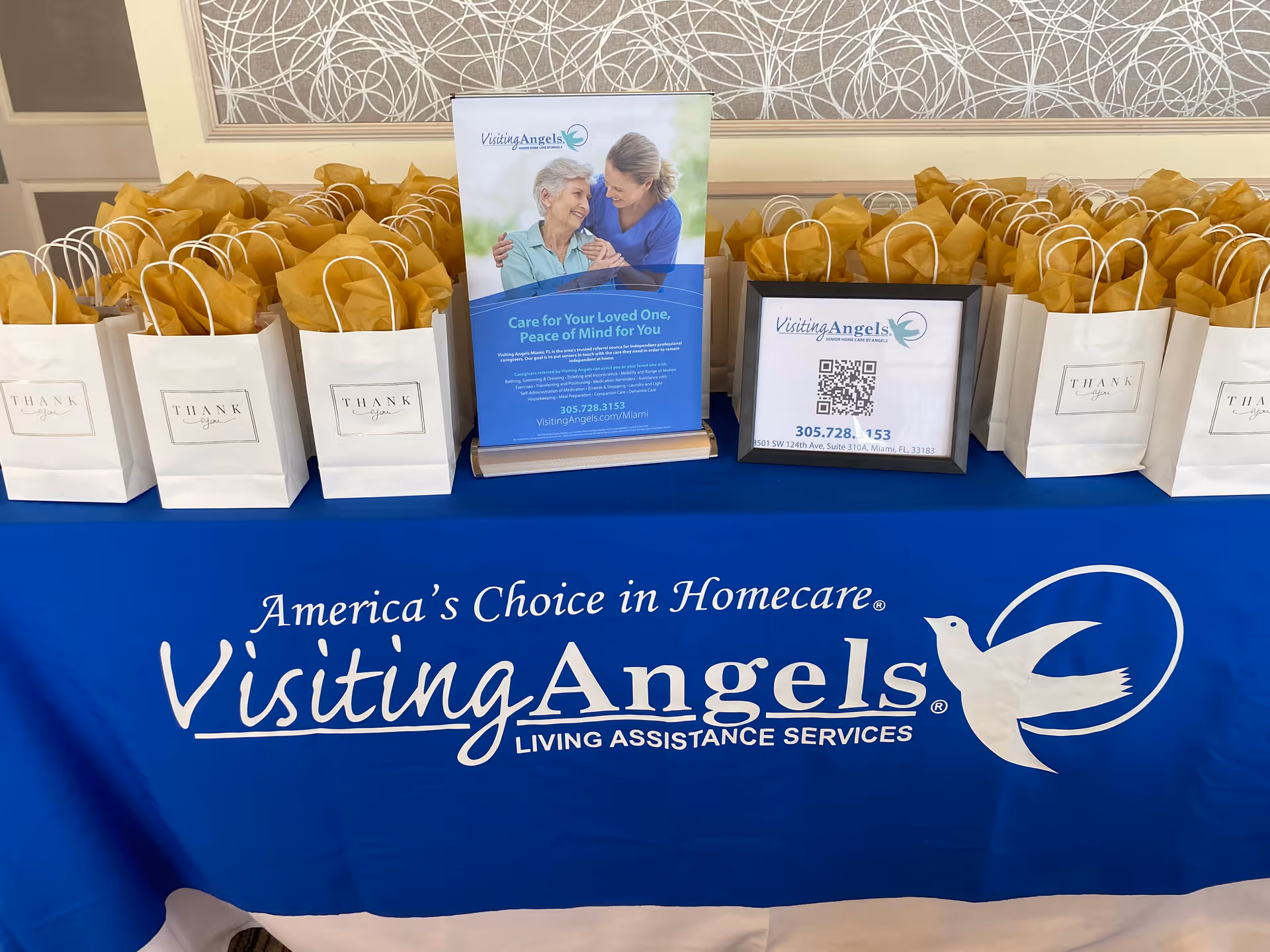 Promotional display on a blue tablecloth with gift bags and Visiting Angels signage