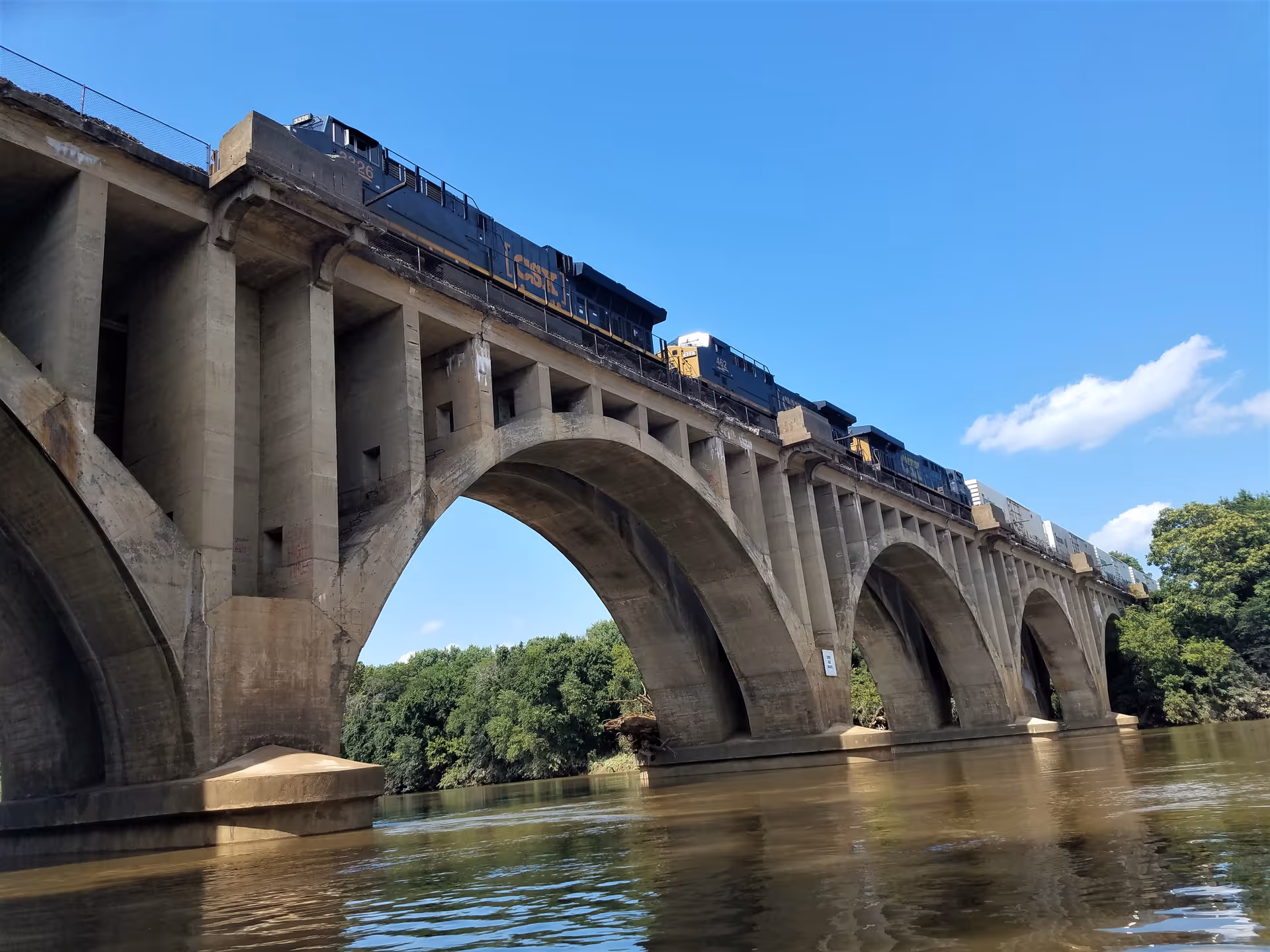 Train crosses a large arched bridge over a calm river.