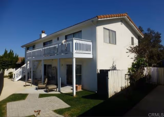 Two-story white senior living building with balcony, stairs, and outdoor seating.