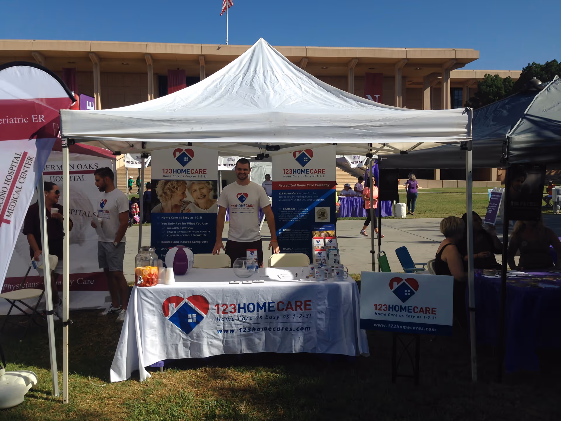 Outdoor 123 Home Care booth at a health fair with banners, tents, and staff.