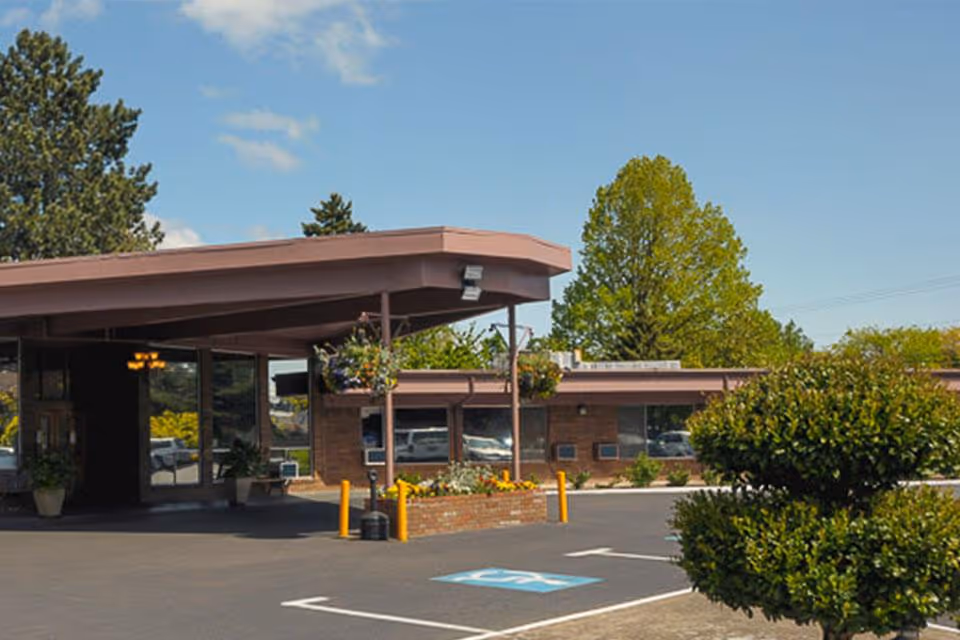 Front entrance of a single-story brick senior living facility with a covered drop-off, parking spaces and landscaping.