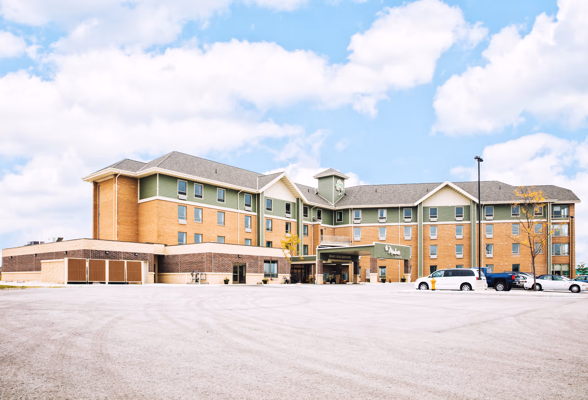 Front view of a multi-story senior living facility with brick exterior and parking area.