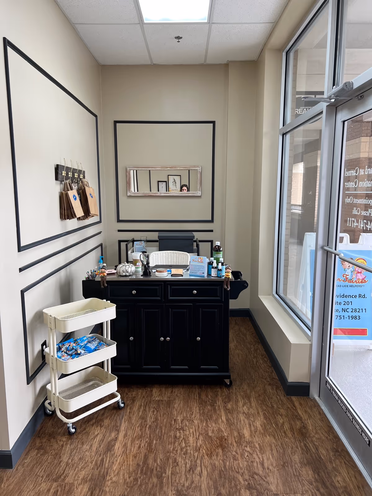 Small reception area with a dark cabinet, cart, and framed mirrors.
