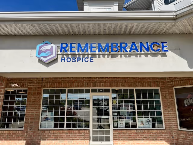 Exterior view of Remembrance Hospice with blue sign, brick facade, and glass entrance.