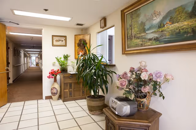 Interior hallway of a senior living facility with potted plants and framed art.