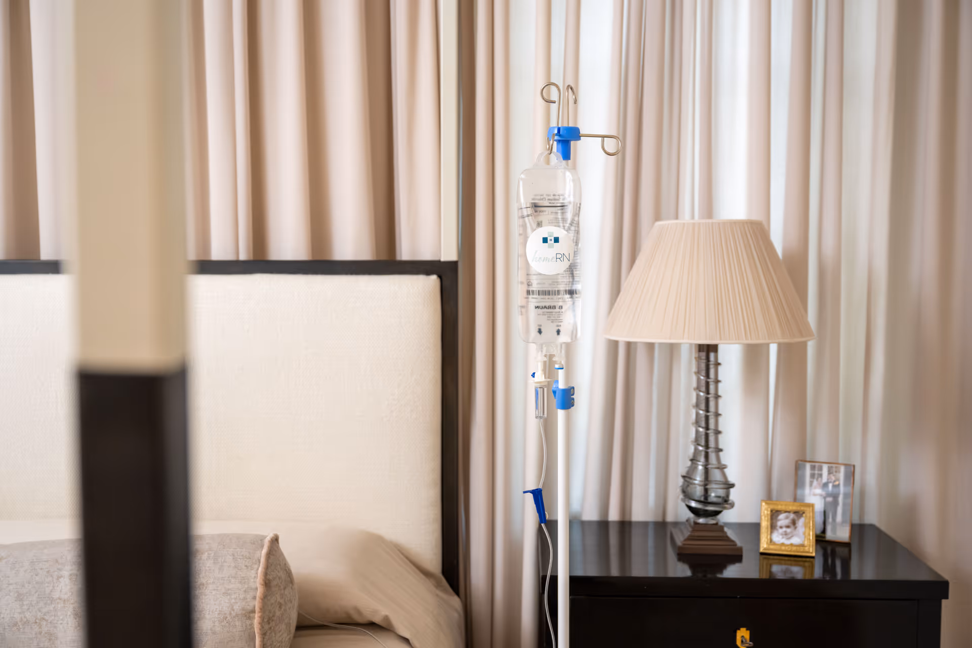 Hospital-style patient bedroom with IV drip, nightstand, lamp, and curtains.