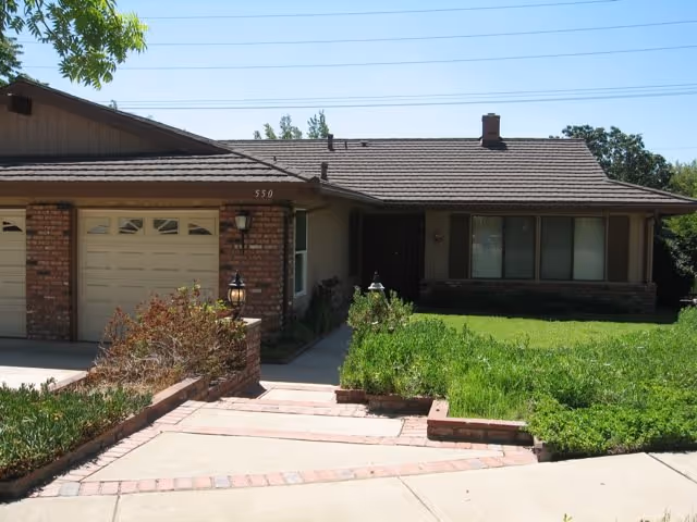 Front view of a single-story brick senior living facility with a driveway and manicured lawn.