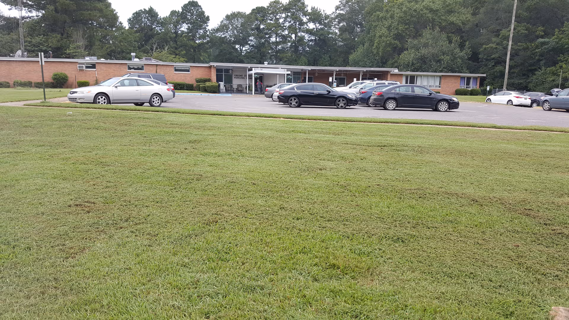 Front exterior of a single-story brick hospital with a parking lot and grassy lawn.