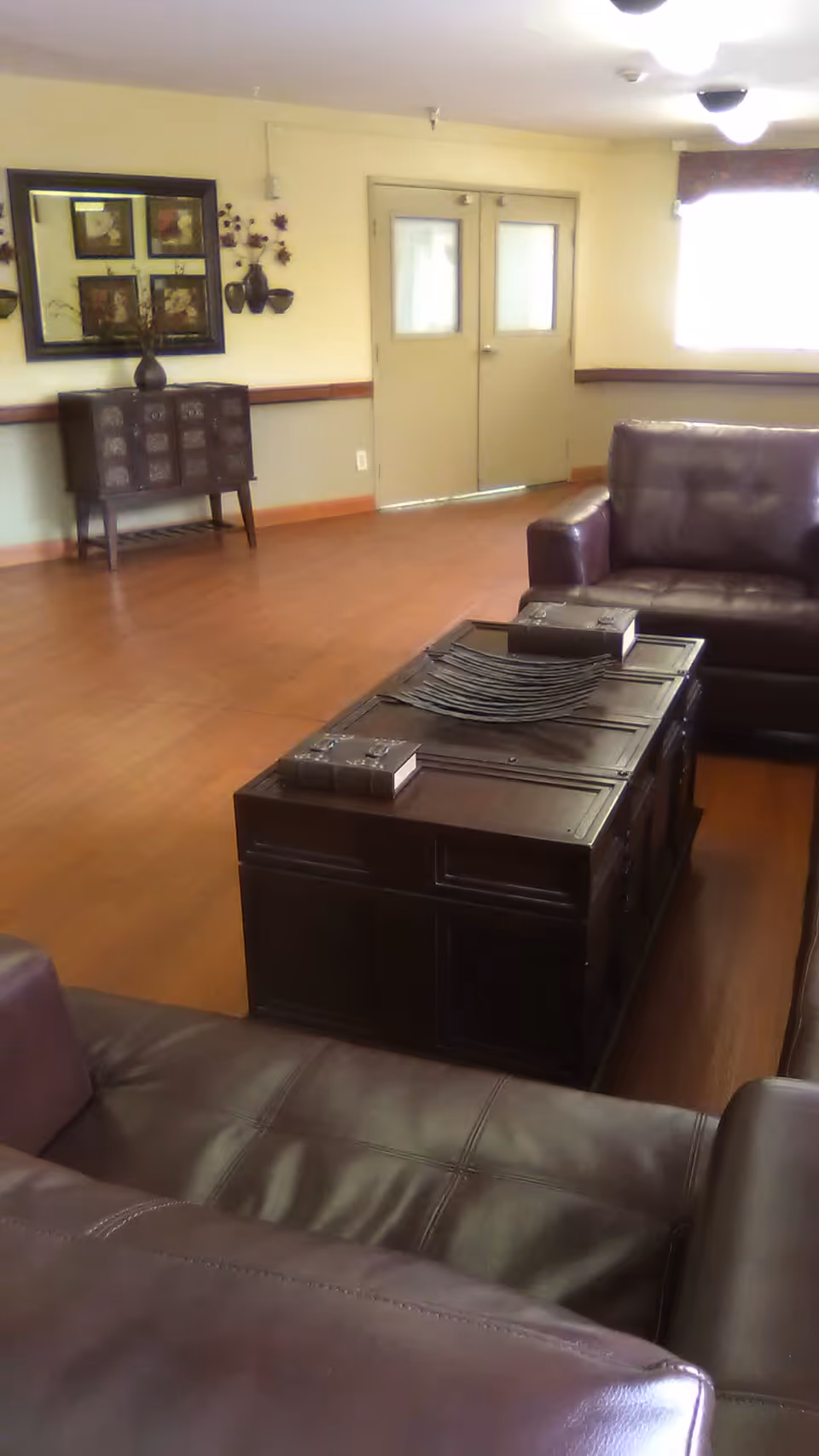 Senior living lounge with brown leather sofas, a coffee table, and wall decor.