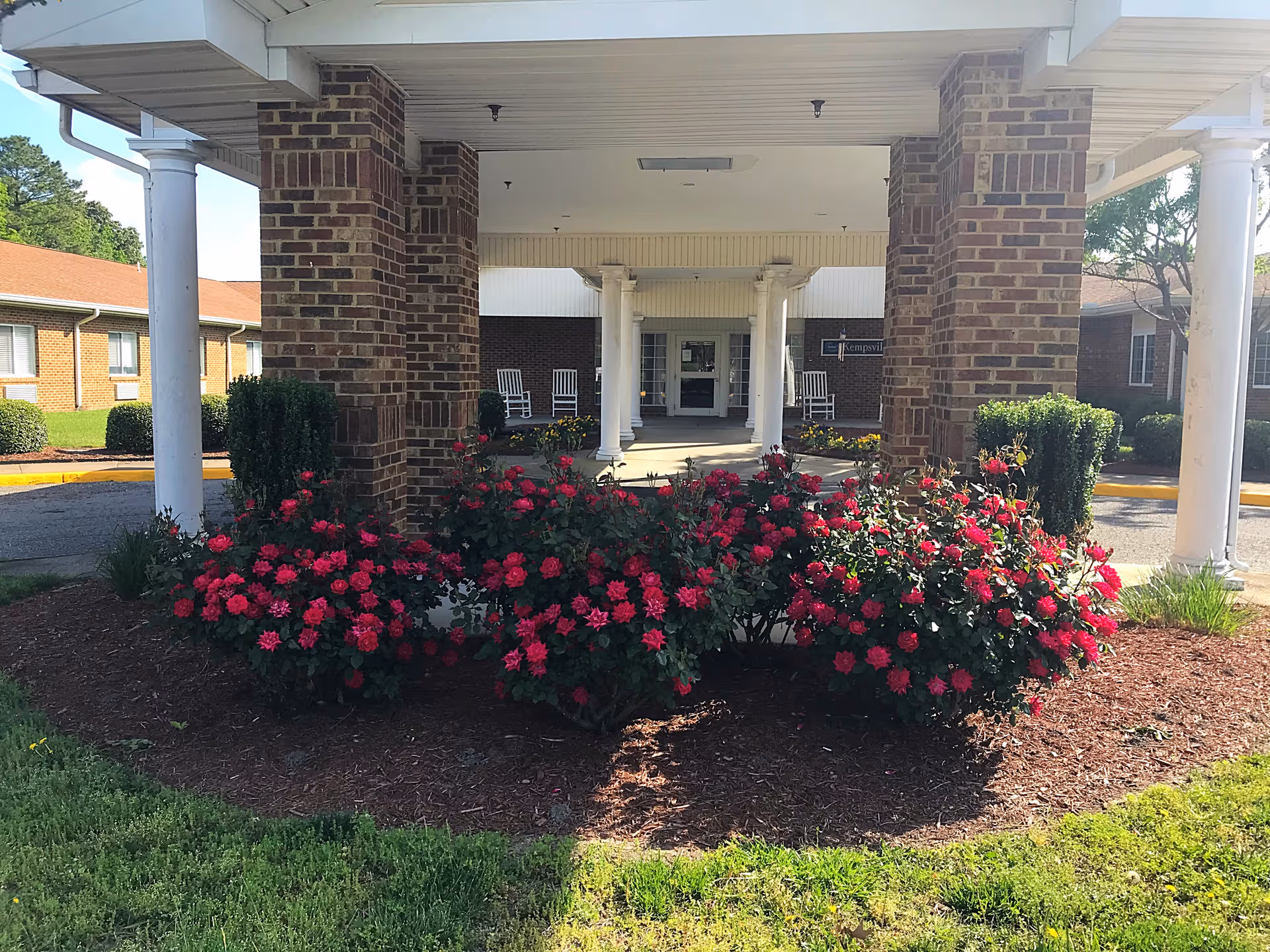 Entrance to Kempsville Health and Rehab Center with brick pillars and red flowers.