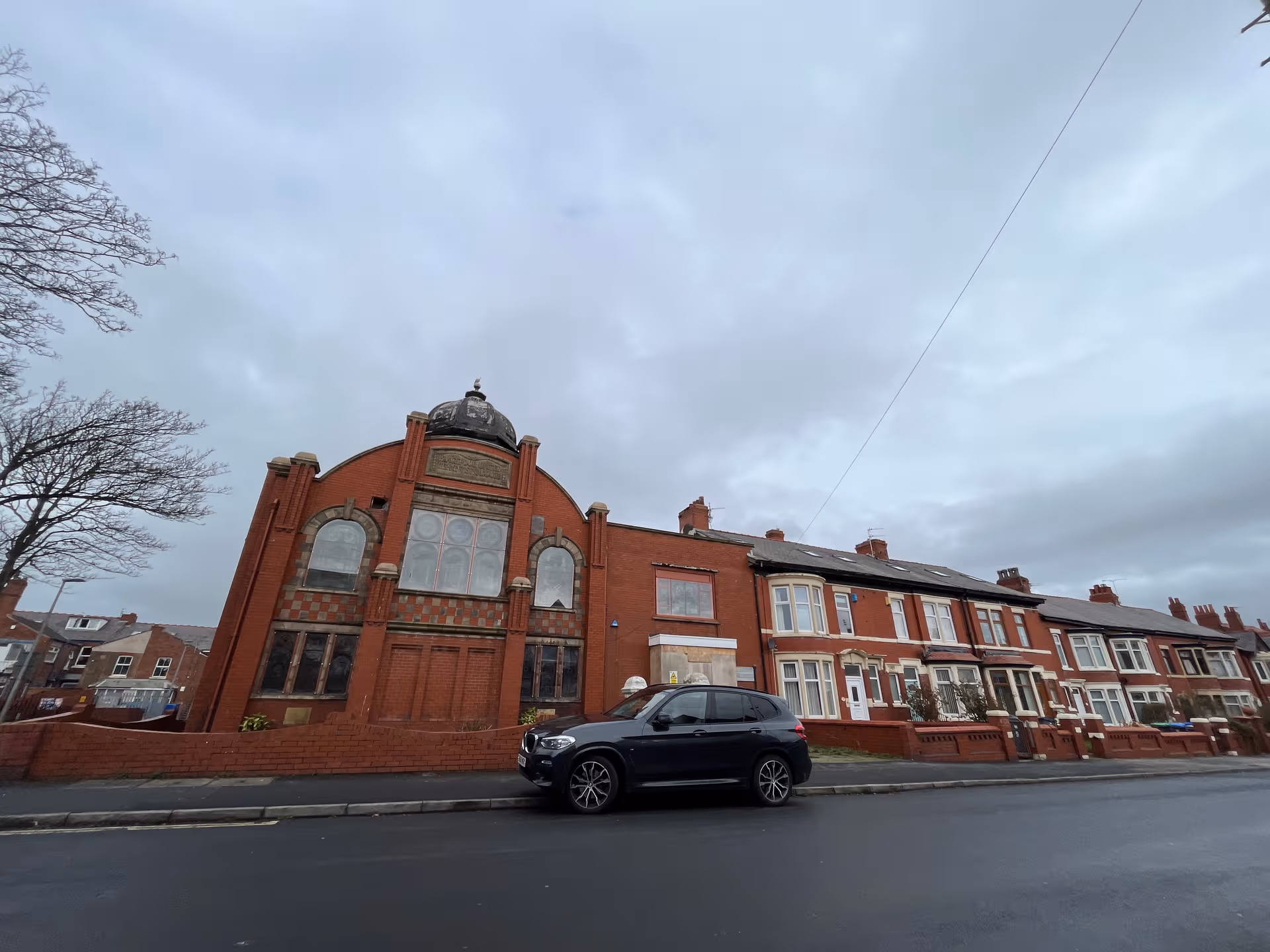Exterior view of a brick building with arched windows along a street; a car parked.