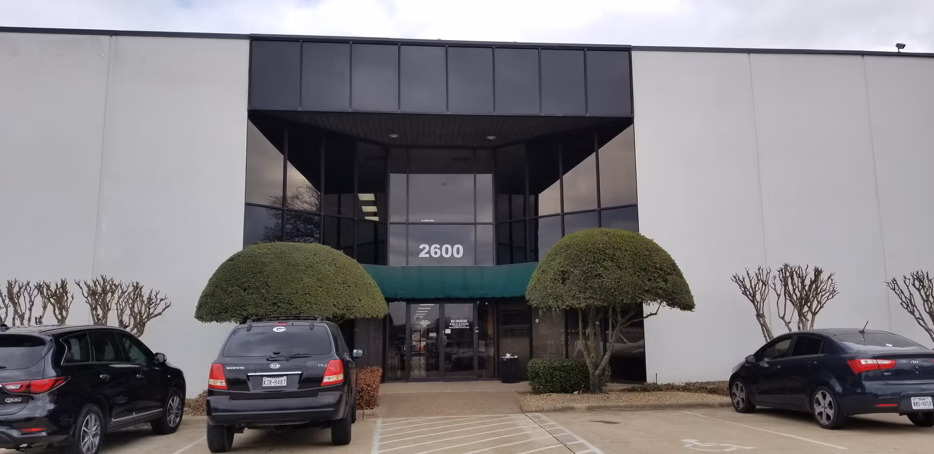 Front exterior of a modern building with glass entrance and parked cars