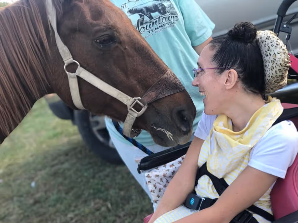 Resident in a wheelchair smiles as a horse nuzzles closely outdoors.