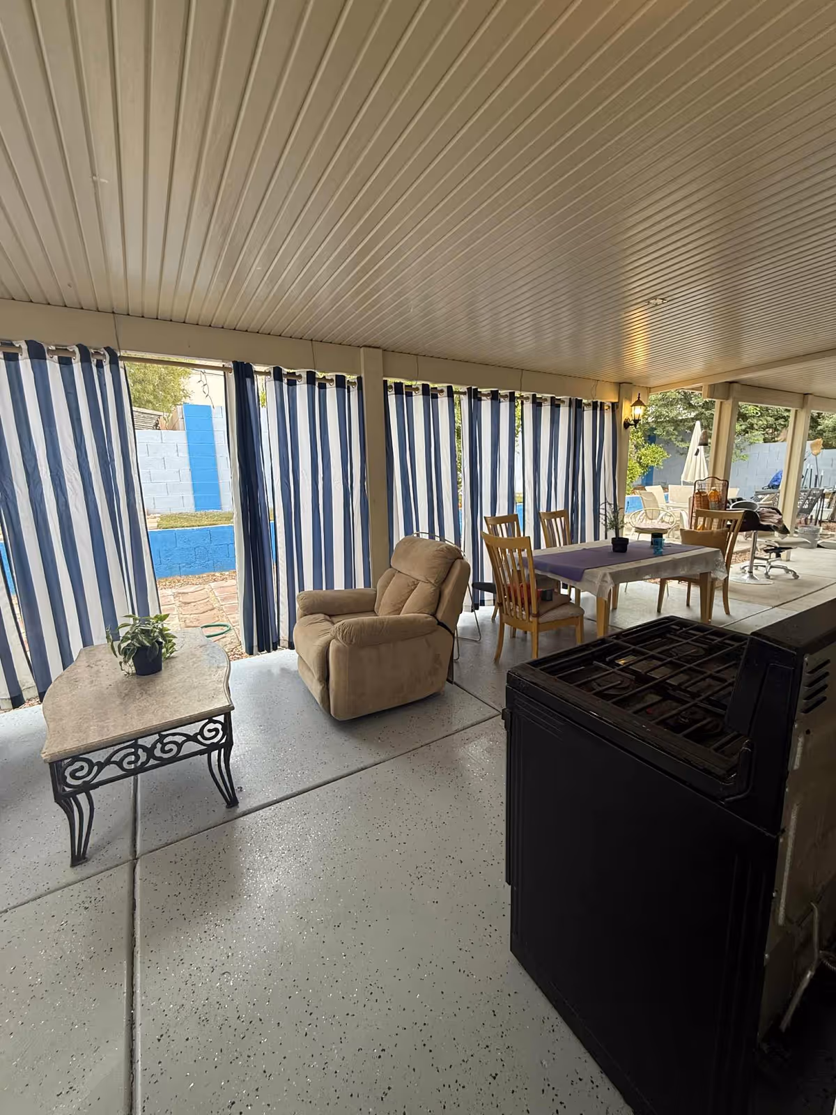 Covered outdoor patio with striped curtains, seating, dining table, and a grill.