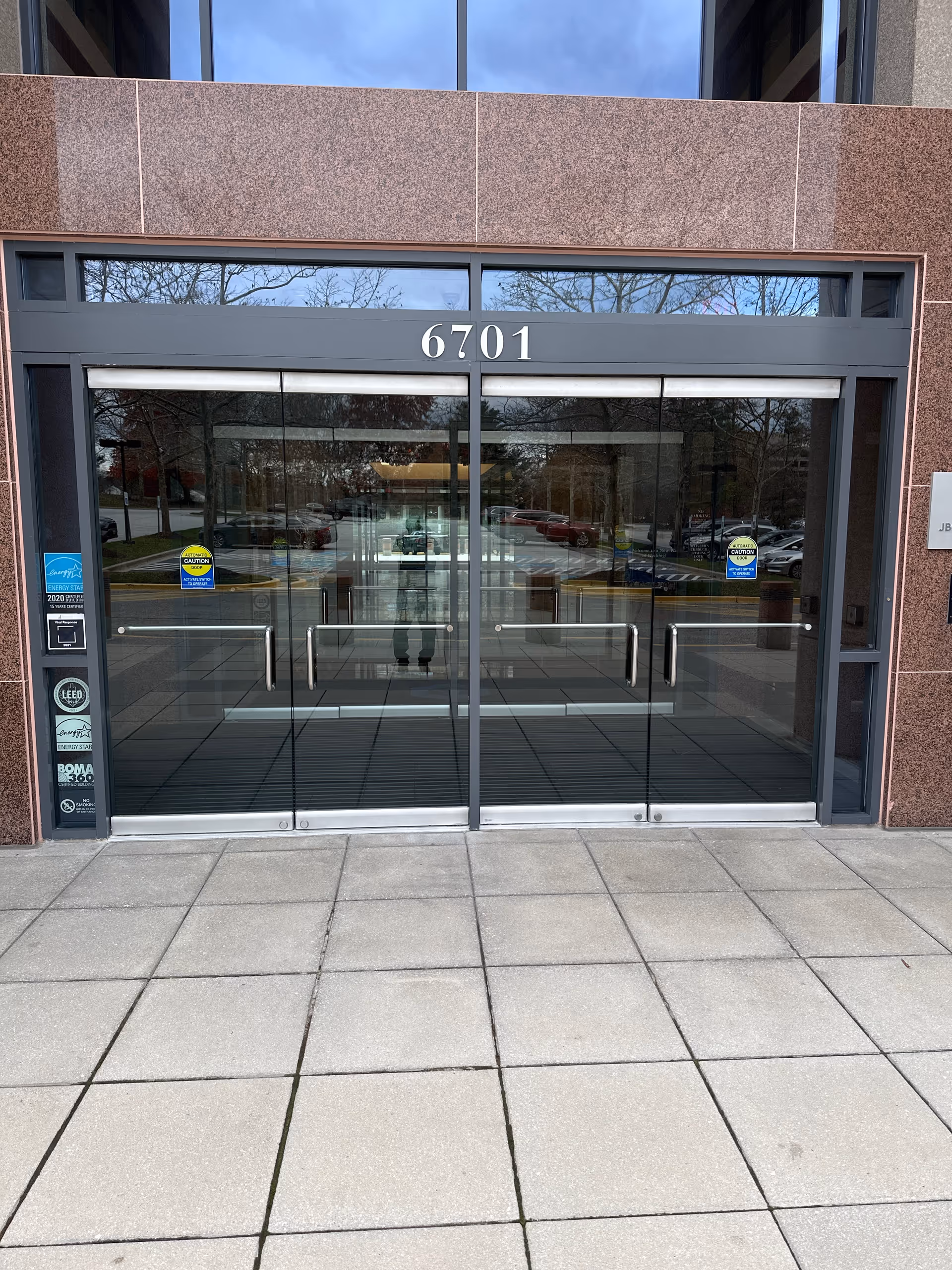 Glass double doors at a brown stone building entrance with the number 6701.