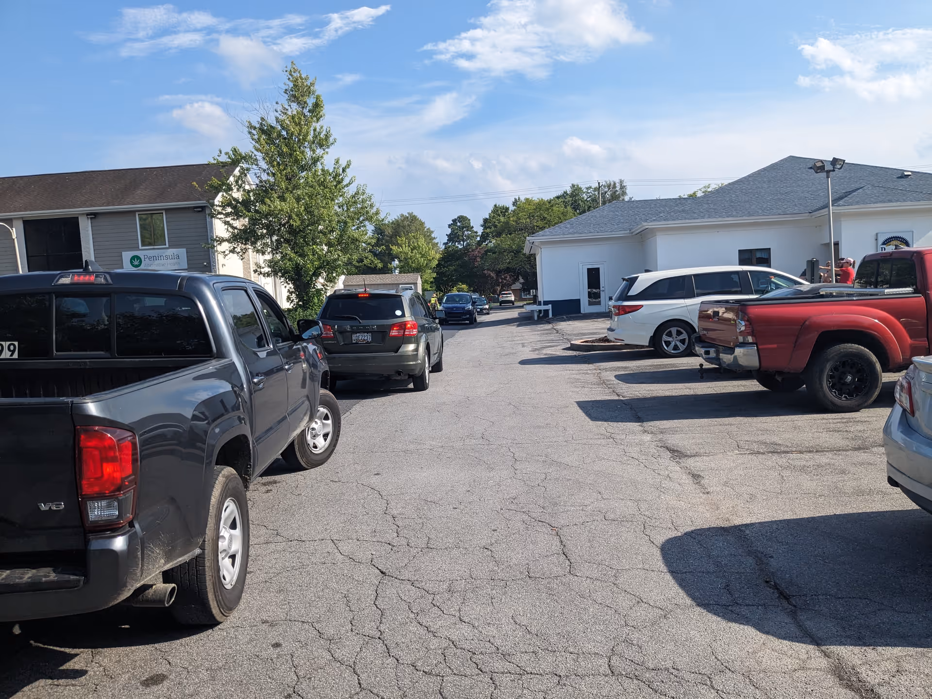 Parking lot in front of a low, white facility with multiple parked cars.