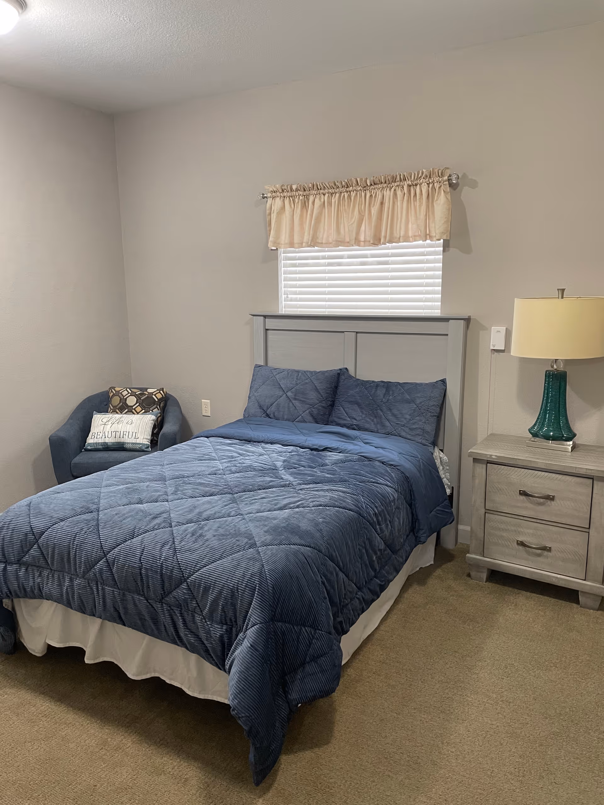 Cozy blue bedroom features a bed, quilted comforter, headboard, nightstand, and lamp.
