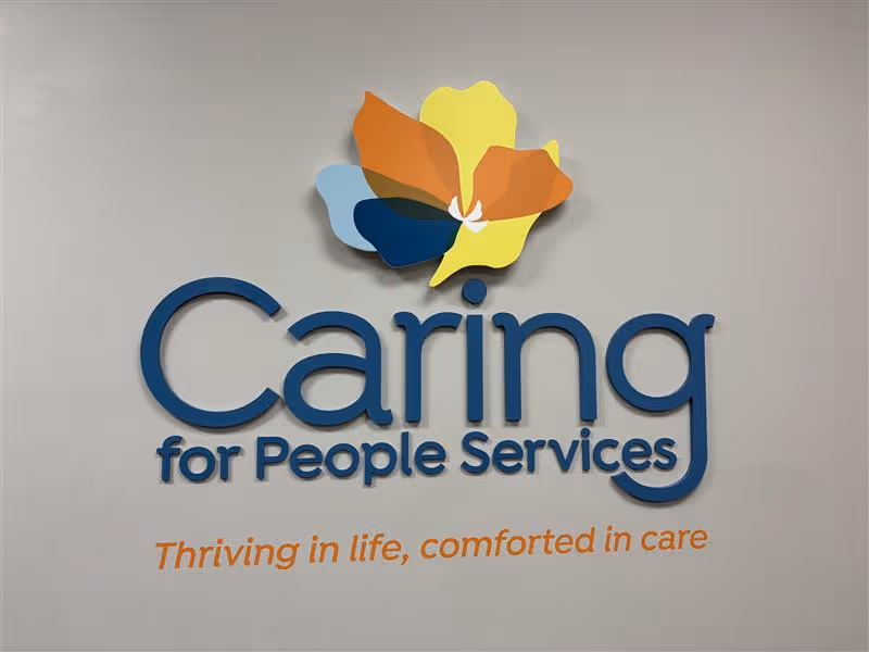 Interior wall sign displaying Caring for People Services with a colorful flower logo.