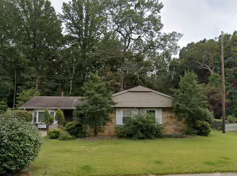 Front exterior view of a single-story assisted living building with trees and lawn.