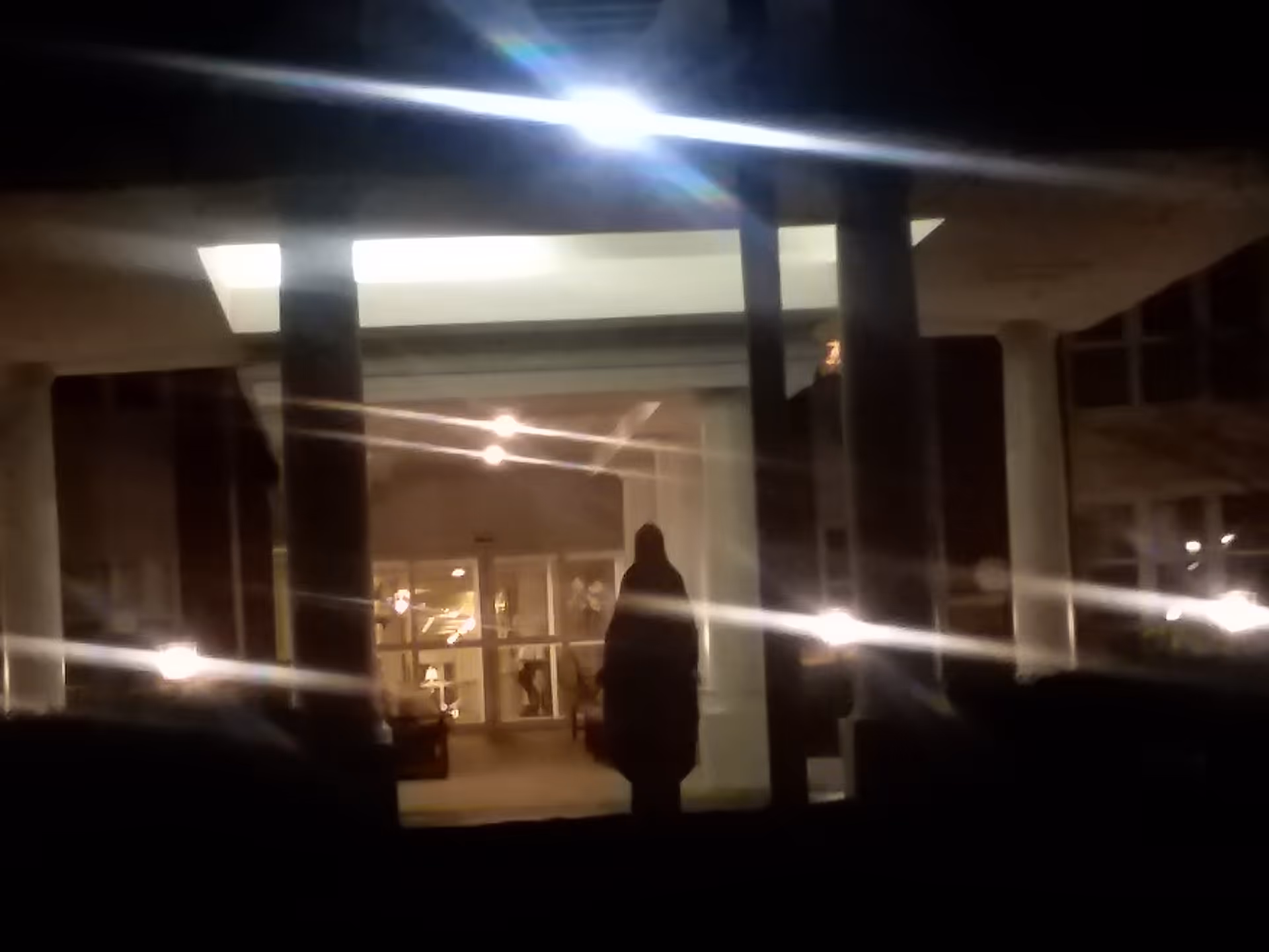 Night exterior view of Our Lady of Peace entrance with a silhouetted person standing.