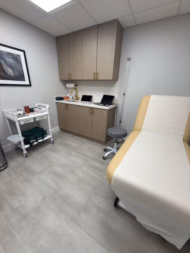 Examination room with a medical chair, cabinets, sink, cart, stools, and IV stand.
