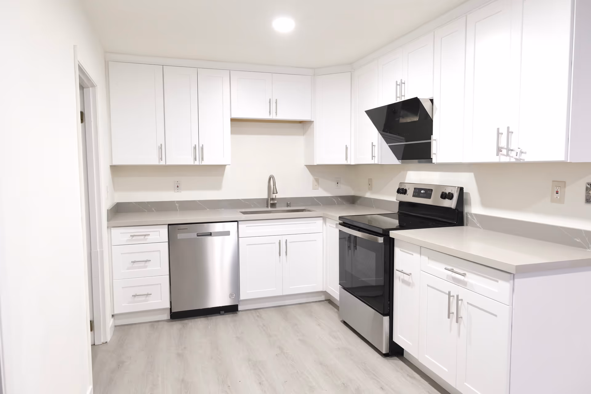 Bright white kitchen with stainless steel appliances, white cabinets, and light gray countertops.