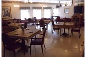 Sunlit senior living dining room with arranged tables, cushioned chairs, and floral centerpieces.
