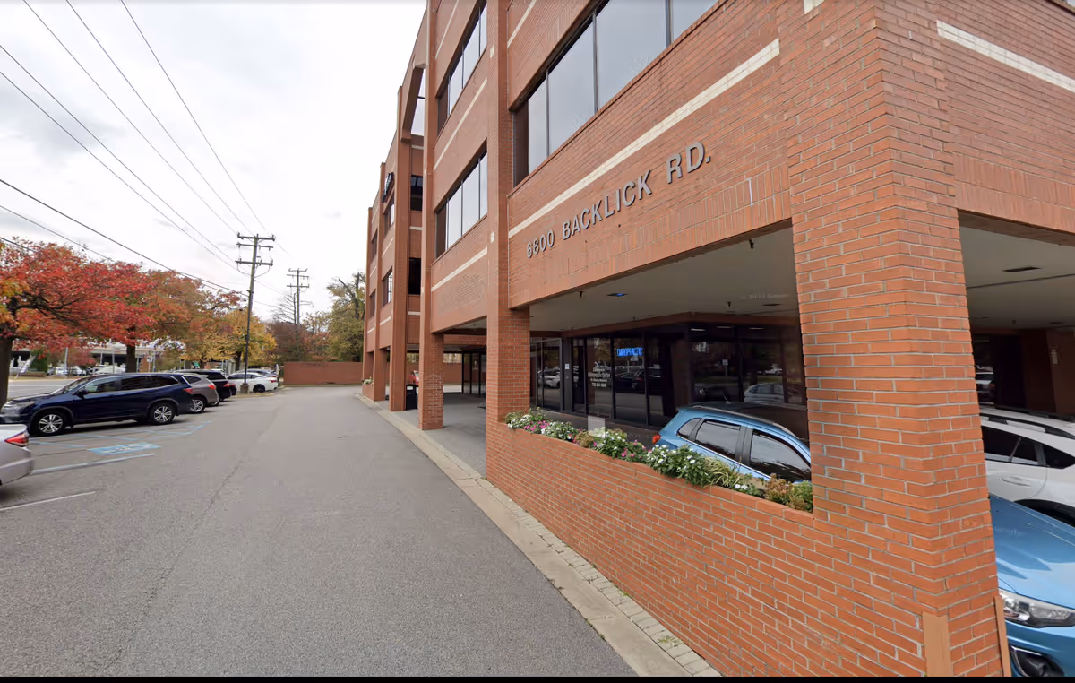 Exterior brick building with windows, a parking lot, and a planter near the entrance.