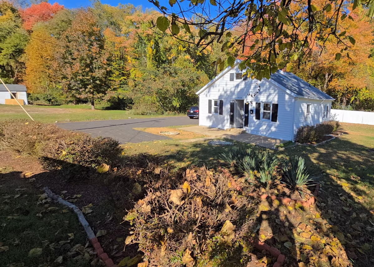 White single-story building with a paved driveway and autumn trees surrounding a yard.