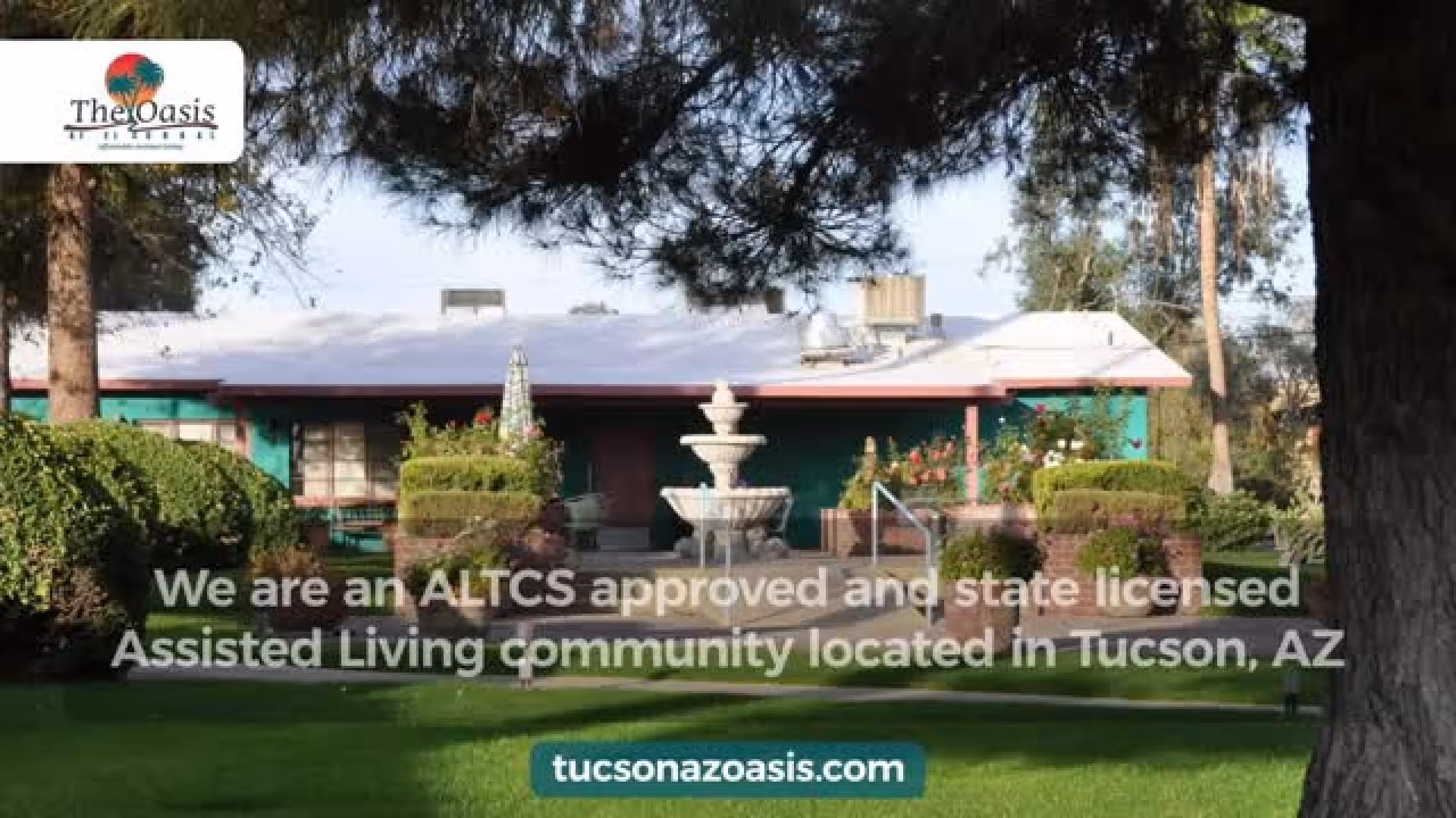 Exterior view of The Oasis Assisted Living Community building surrounded by trees, bushes, and a green lawn with a central water fountain in front.