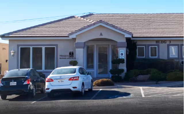 Front view of a single-story medical clinic with parked cars and shrubs.