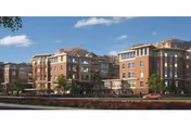 Multi-story brick senior living building with balconies, landscaped grounds, and mountains in the background under a blue sky.