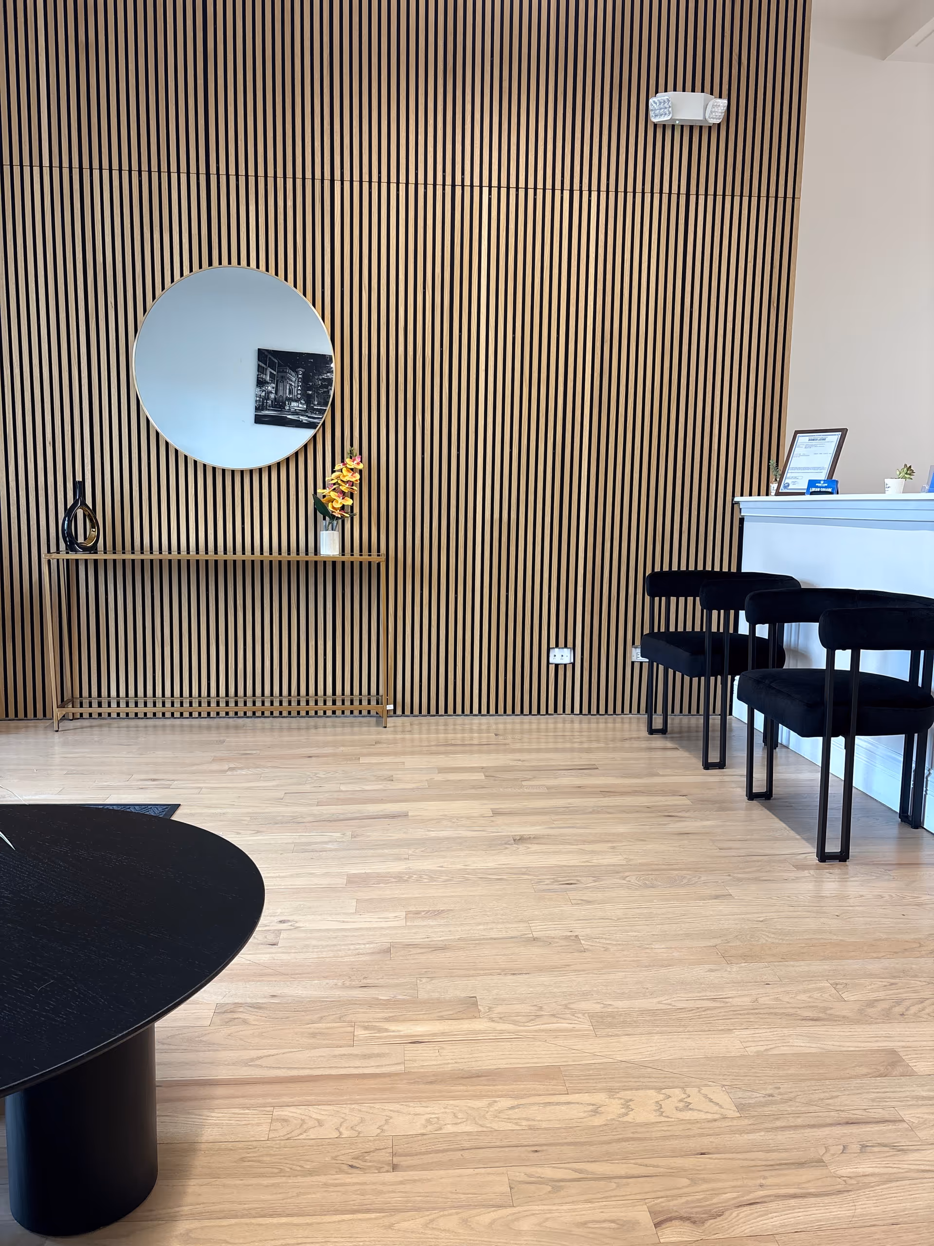 Modern reception area with wood slat wall, round mirror, console table, and black chairs.