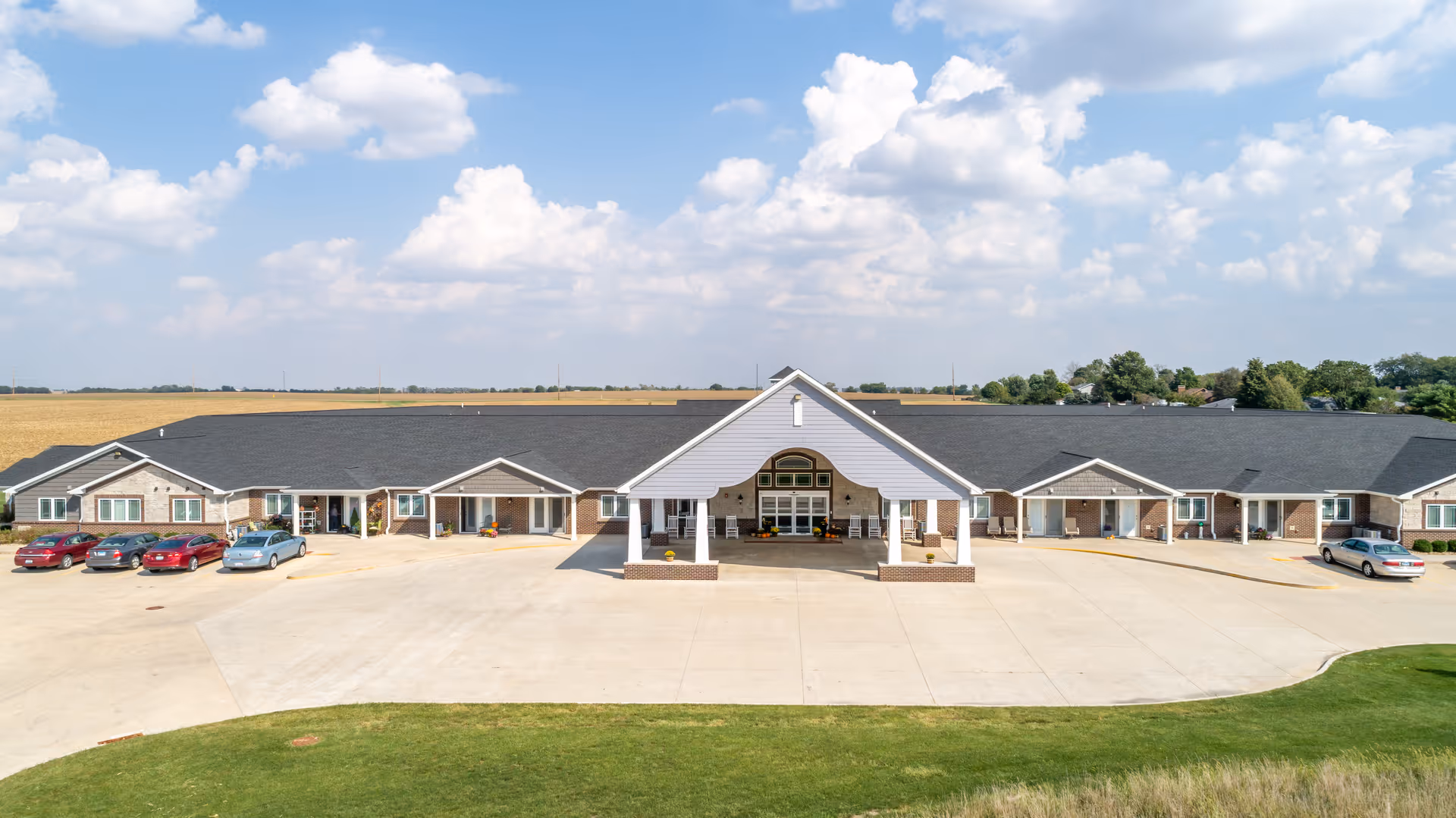 Wide view of Reflections Memory Care Herrin building exterior with a large parking lot.