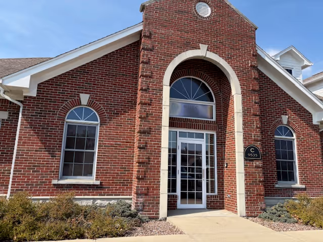 Brick senior living facility entrance featuring arched doorway and large windows.