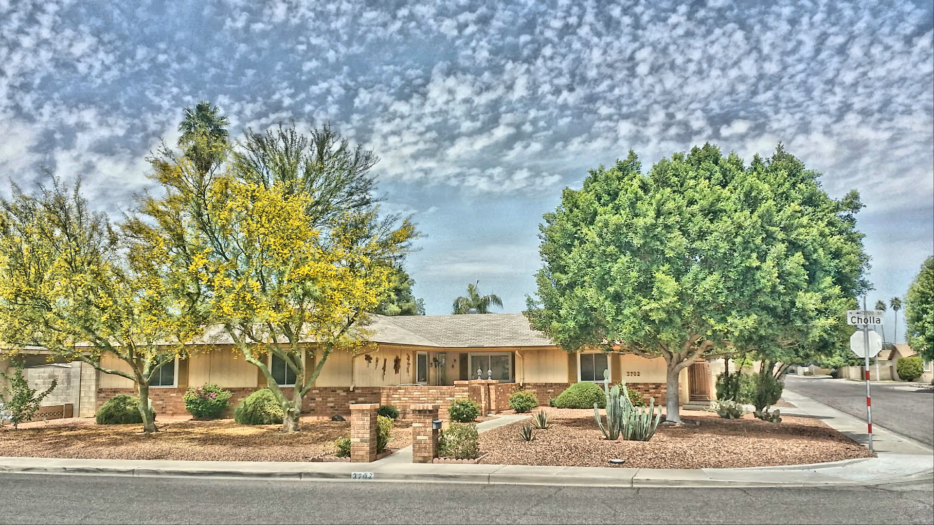 Exterior view of a single-story assisted living home with desert landscaping and trees.