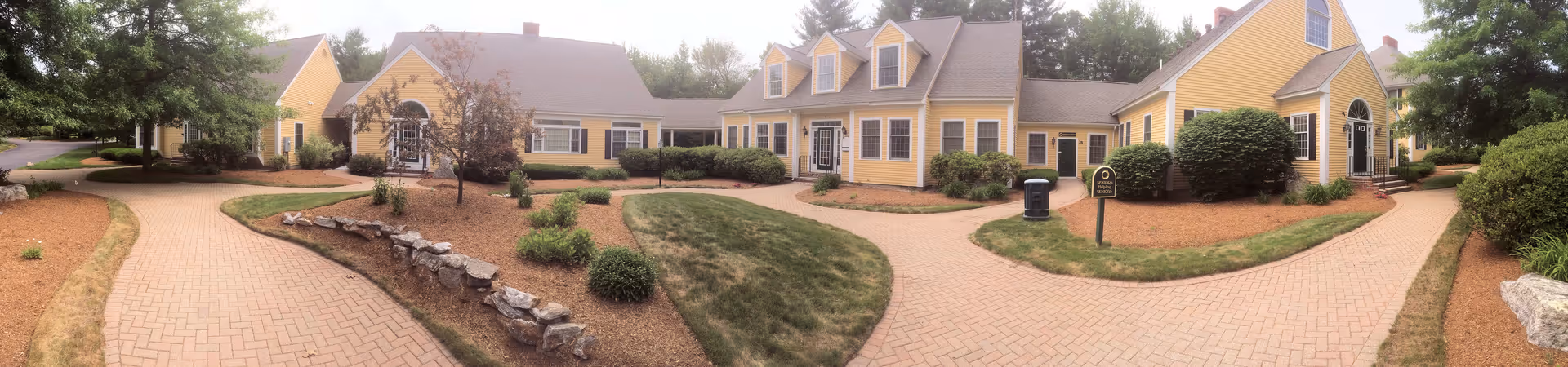 Panoramic view of a yellow senior living campus with brick walkways and landscaping.