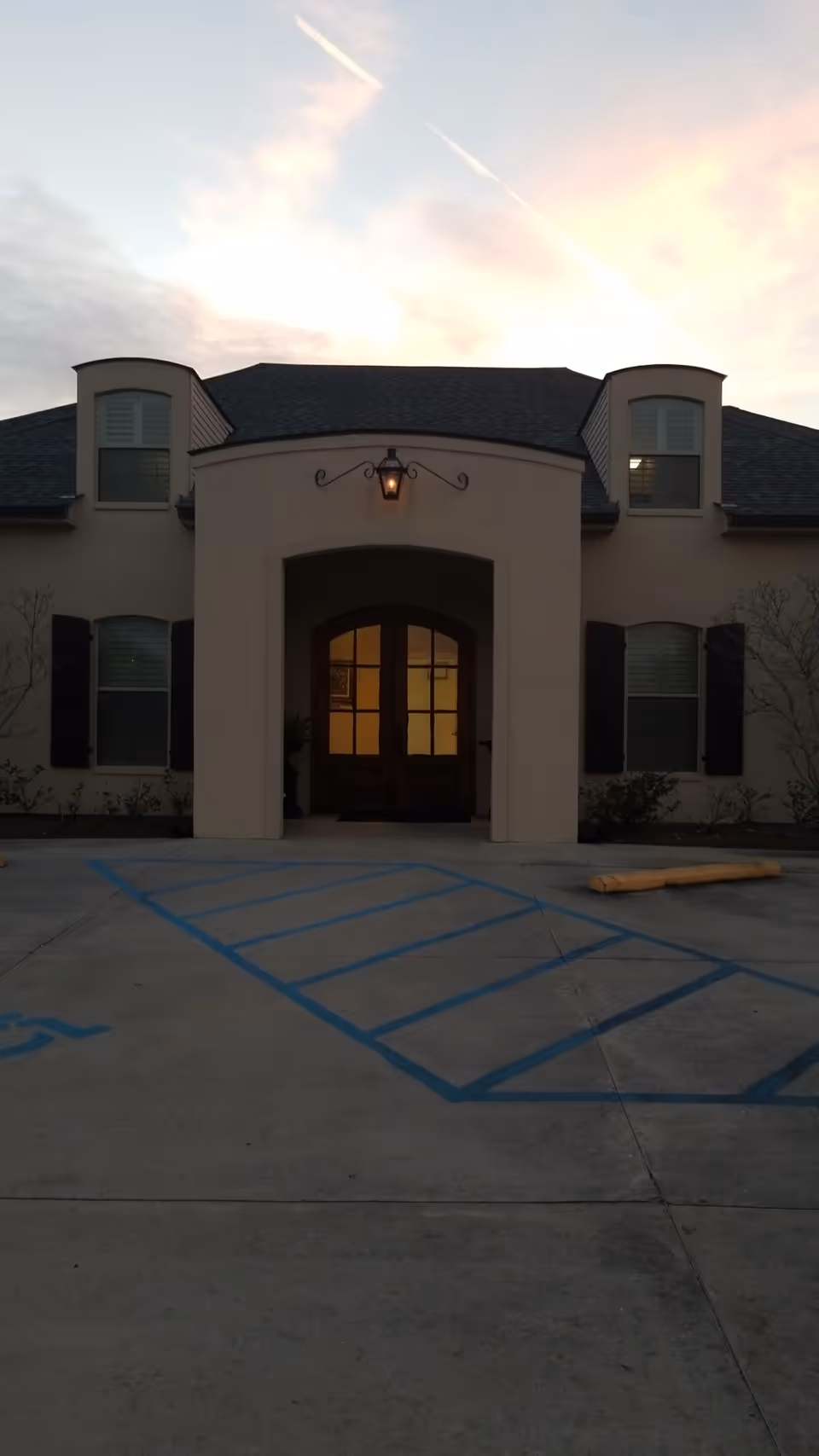 Front entrance of a beige senior living facility with double doors and a parking lot.